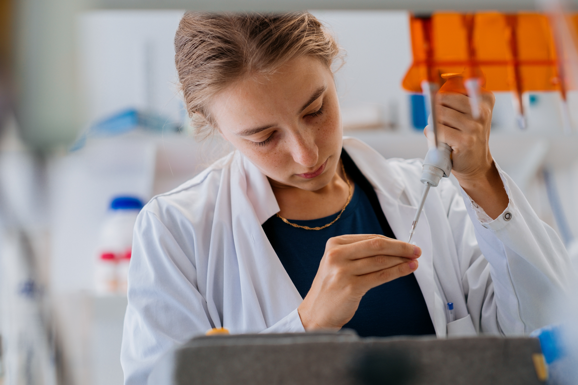 A woman in a white lab coat uses a pipette.