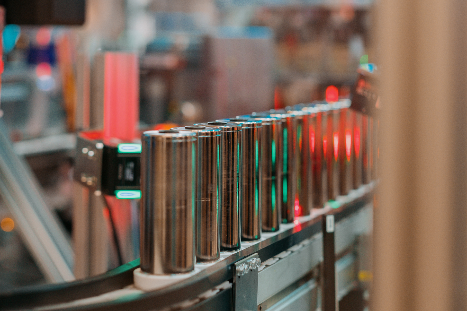 A row of shiny cylinders on a small conveyor belt in a complex machine that glows with red and blue lights.