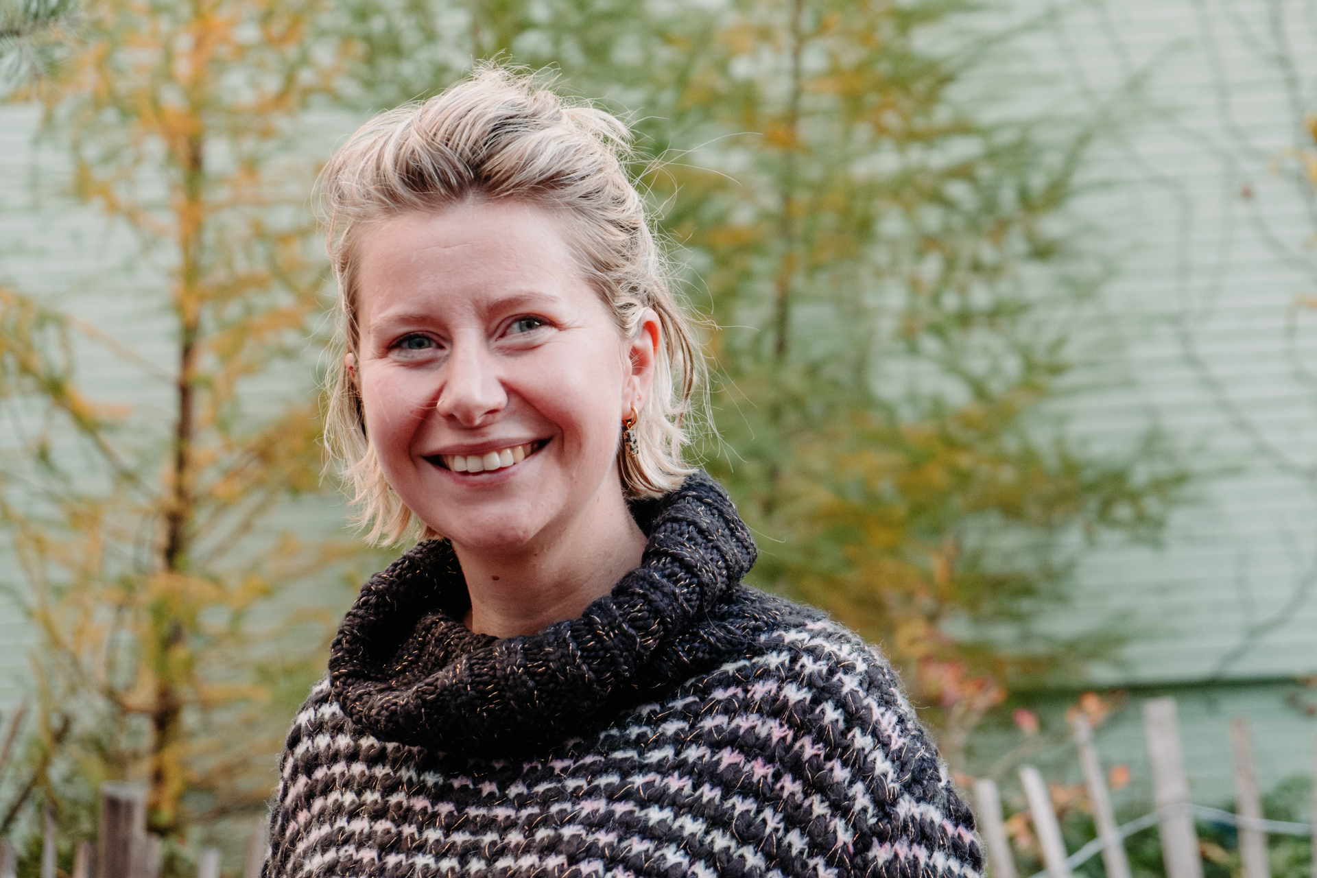 Head-and-shoulders portrait of a smiling blonde woman in a gray-and-white pattered sweater. 