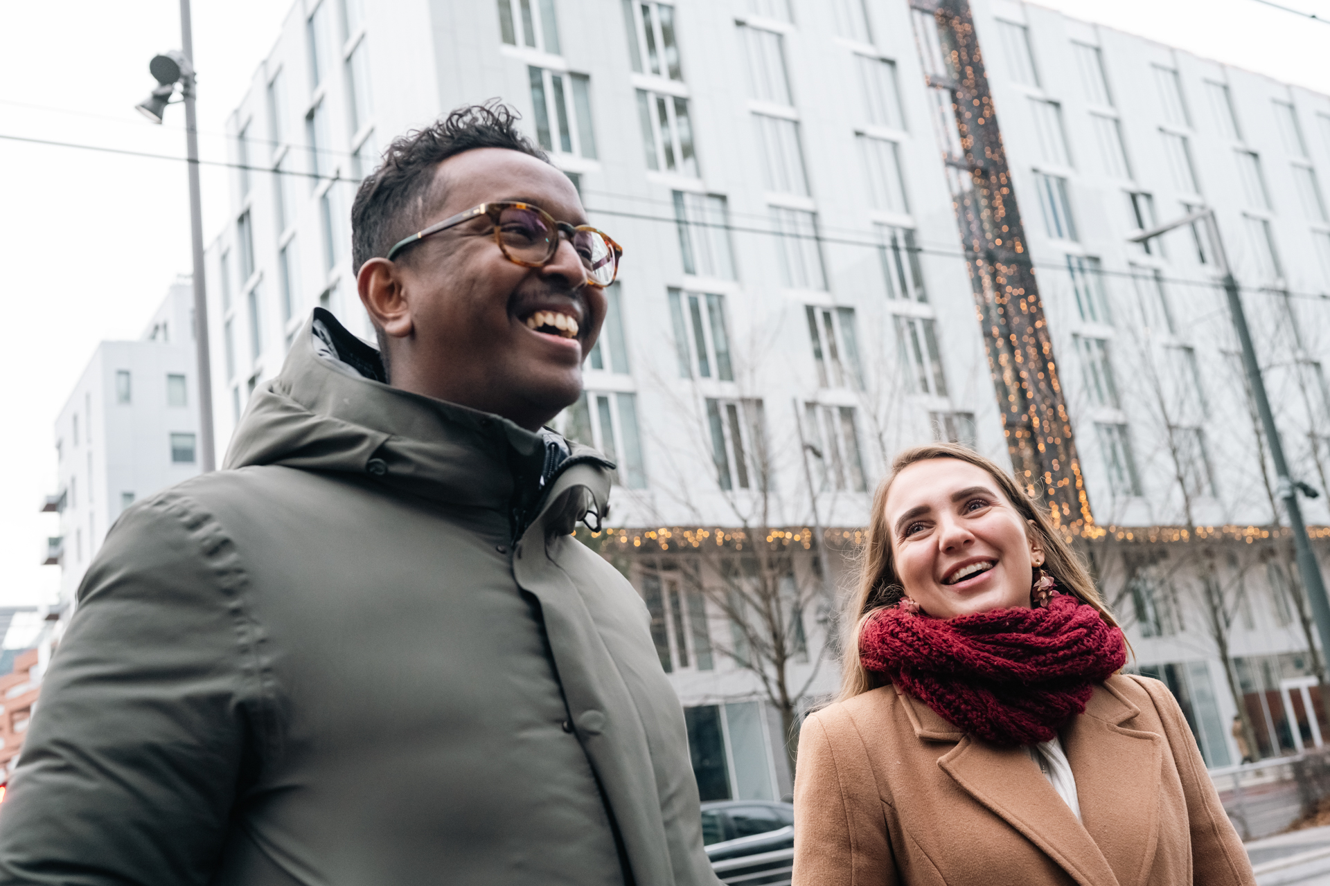 A smiling man, left, and woman wearing winter clothes on a city street.