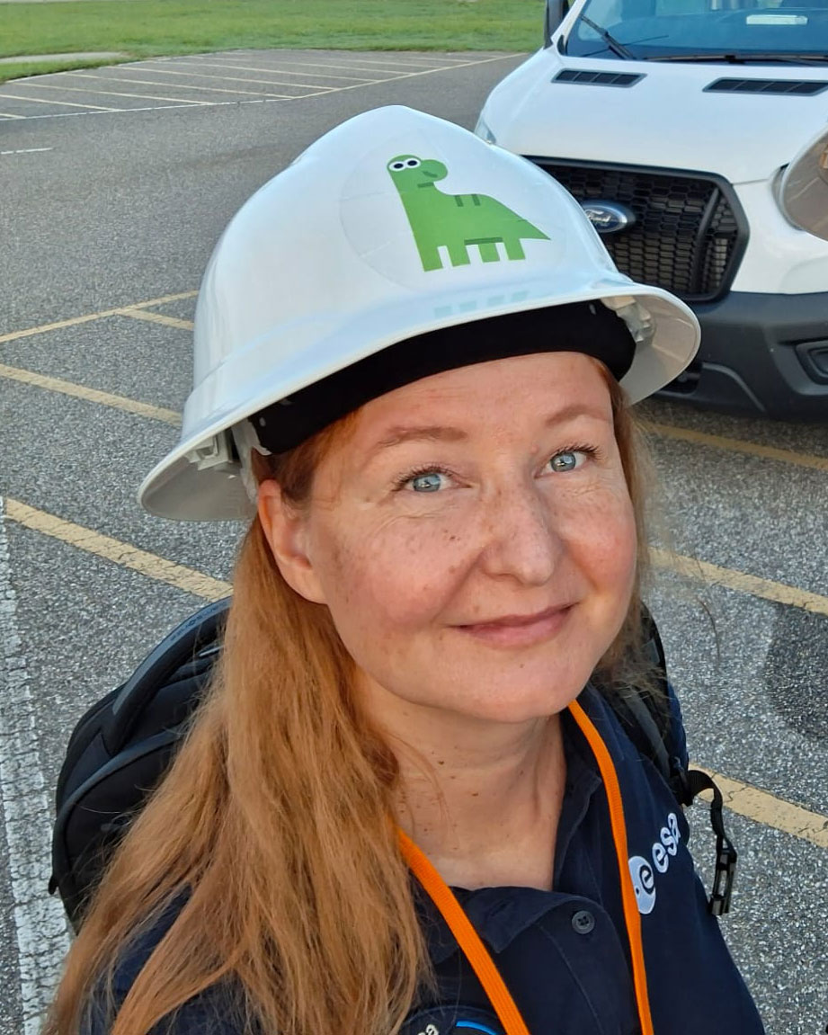 Woman with bright blue eyes in a hardhat with a dinosaur on it seen from above.